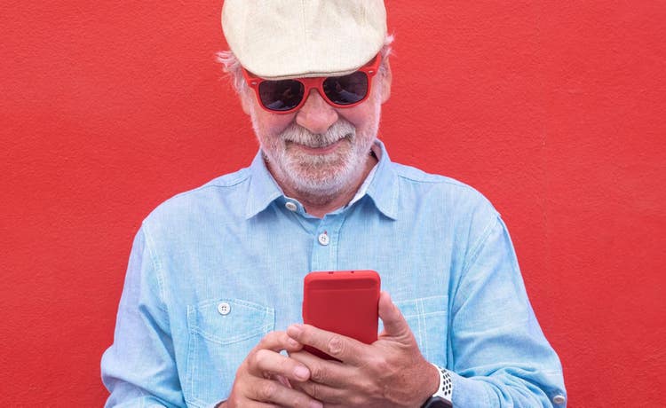 older man looking at smartphone with a red background and wearing sunglasses