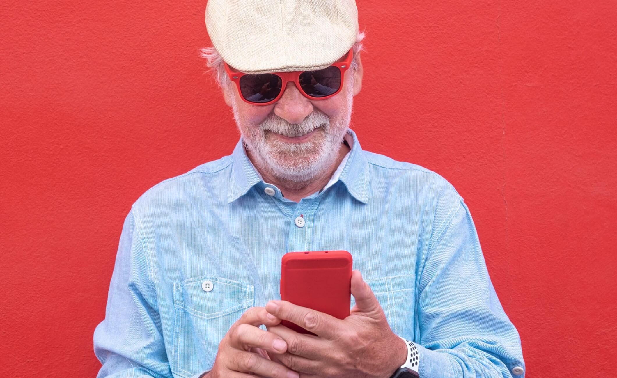 older man looking at smartphone with a red background and wearing sunglasses