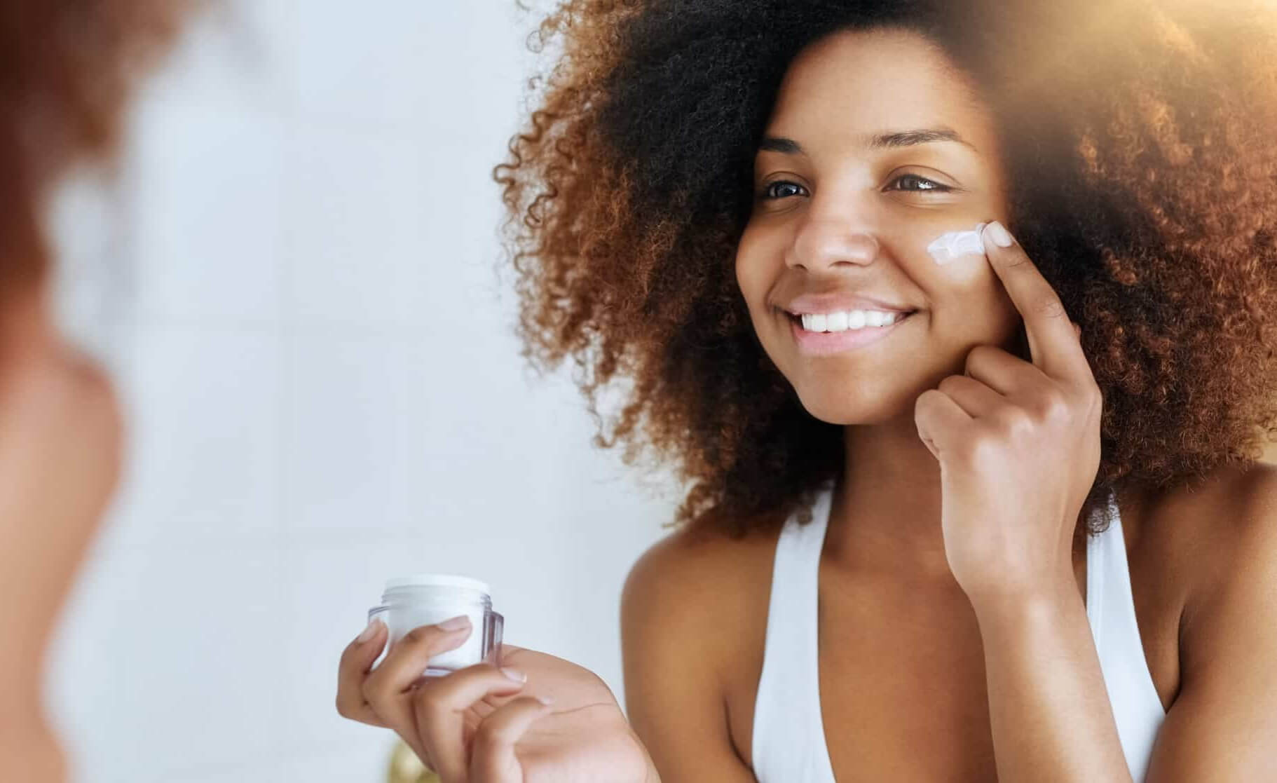 Woman smiling while looking mirror and applying face cream
