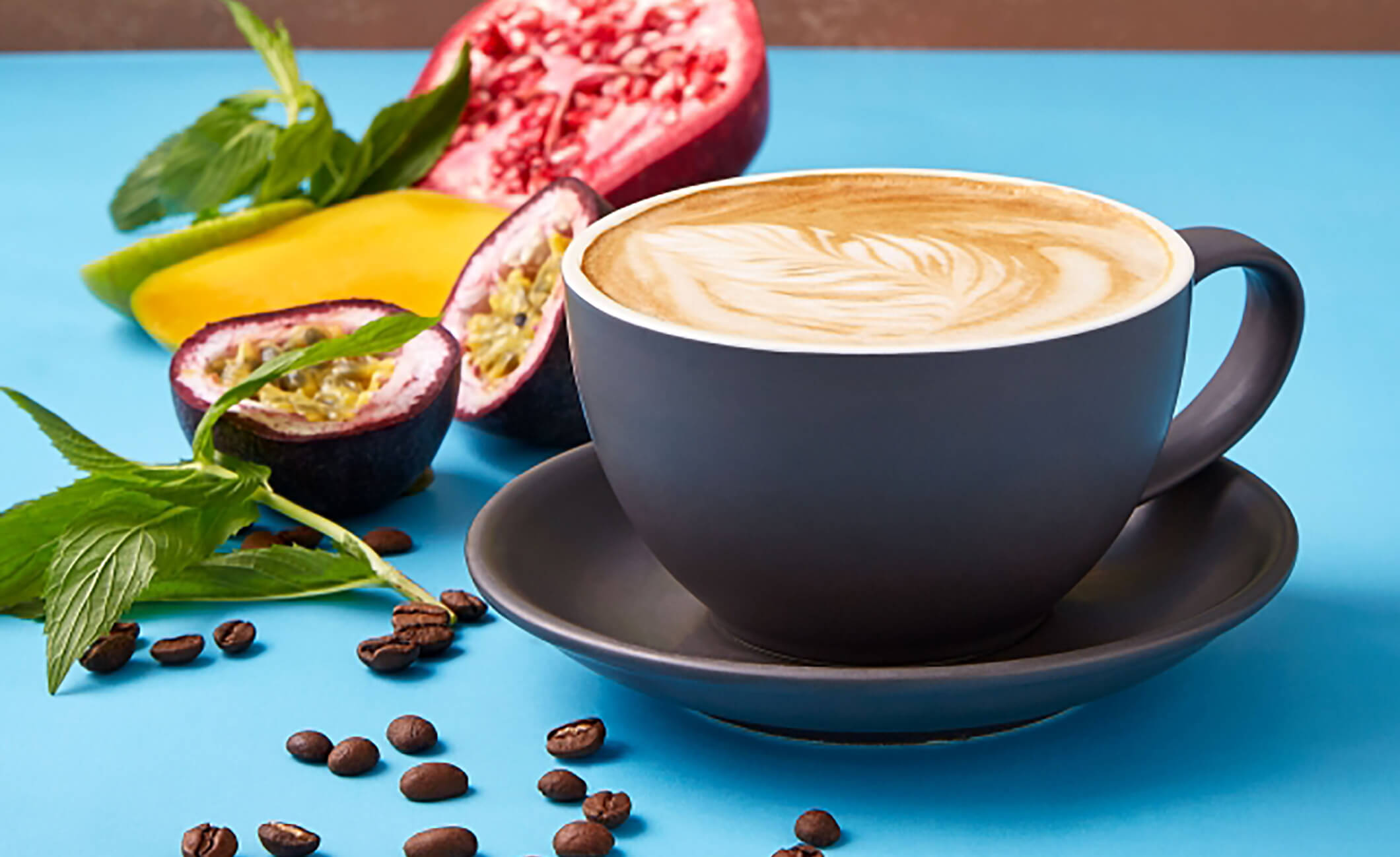 Coffee in blue mug next to scattered coffee beans and fruit